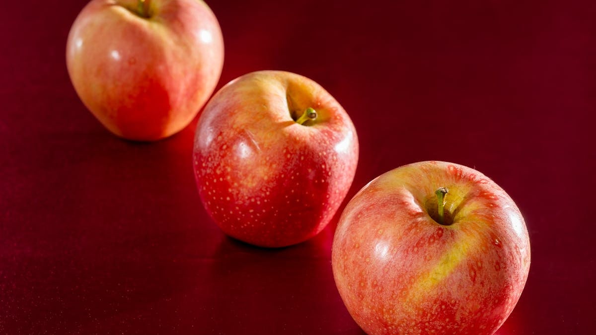Three fresh red apples on a deep red background emphasizing health and vitality.